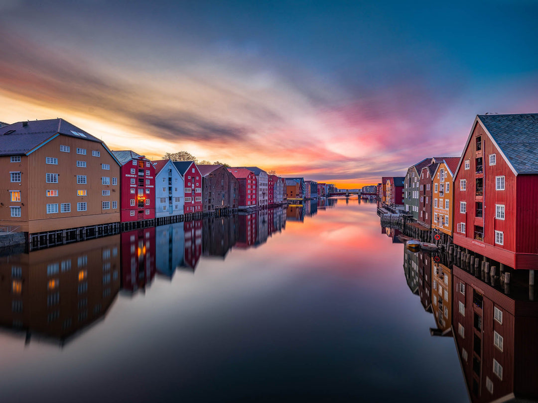 Vibrant photo of Trondheim's waterfront at sunset, featuring colorful buildings reflected in the Nidelva River, part of the Trondheim Wall Art Collection.