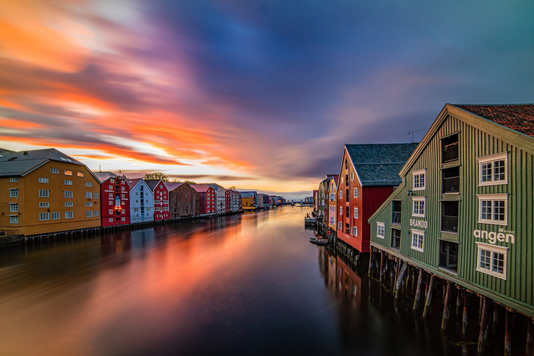Colorful wooden buildings, Bryggene, reflected in the calm Nidelva River at sunset in Trondheim, Norway